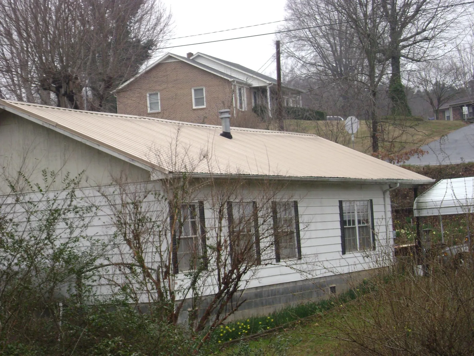 Tan metal roof on a white sided house set into a hillside — Commercial Roofing by Roofing Brothers in Salem